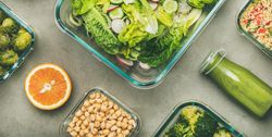 Variety of vegetable dishes in glass containers with bottles of dressing, wide composition