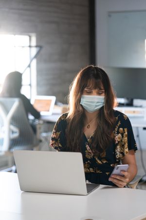 Transgender woman wearing a face mask and checking smart phone at her desk