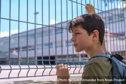 Boy holding fence looking into school yard 4djXA0