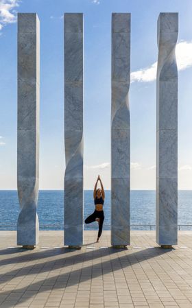 Woman standing on one leg between sculpture with ocean view 