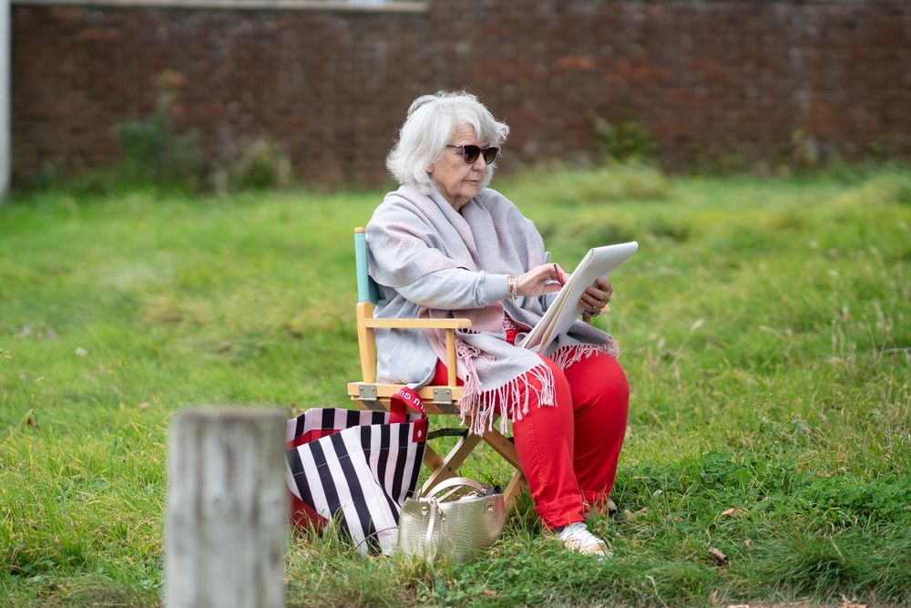 Older woman sitting outside in park at drawing class in sunglasses