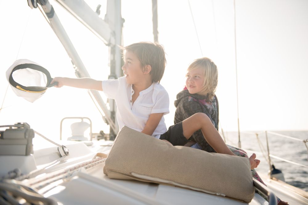 Smiling children sitting on edge of yacht in sea