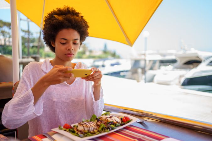 Woman using phone take picture of meal at waterfront cafe