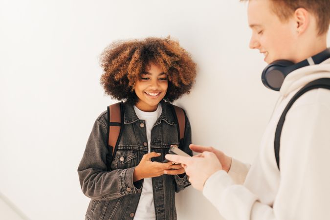 Male and female checking phones and smiling in school corridor