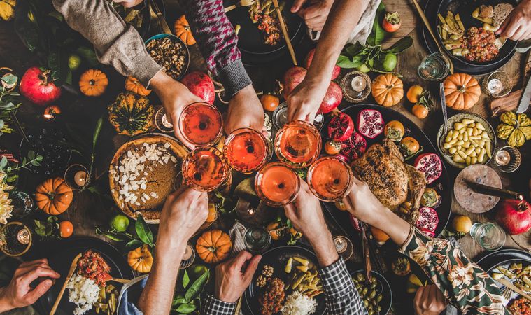 Group of people toasting wine glasses at festive table with roast chicken, squash and pie