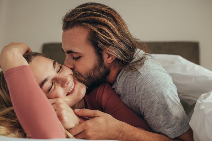 Affectionate man kissing his wife while sleeping on bed