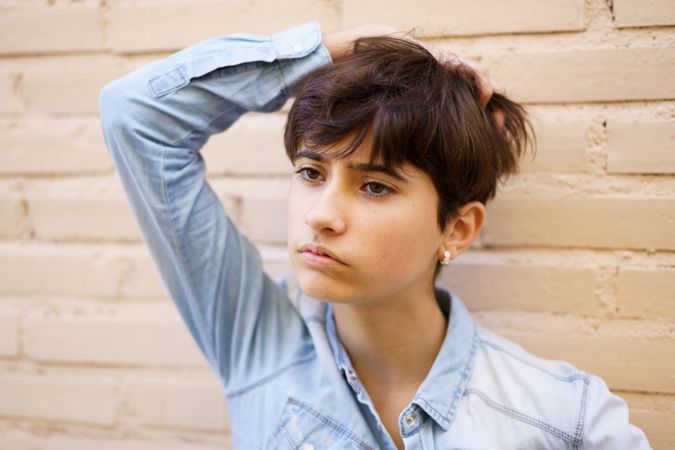 A Thoughtful Young Individual Featuring Short Hair, Posing Elegantly Against a Brick Wall
