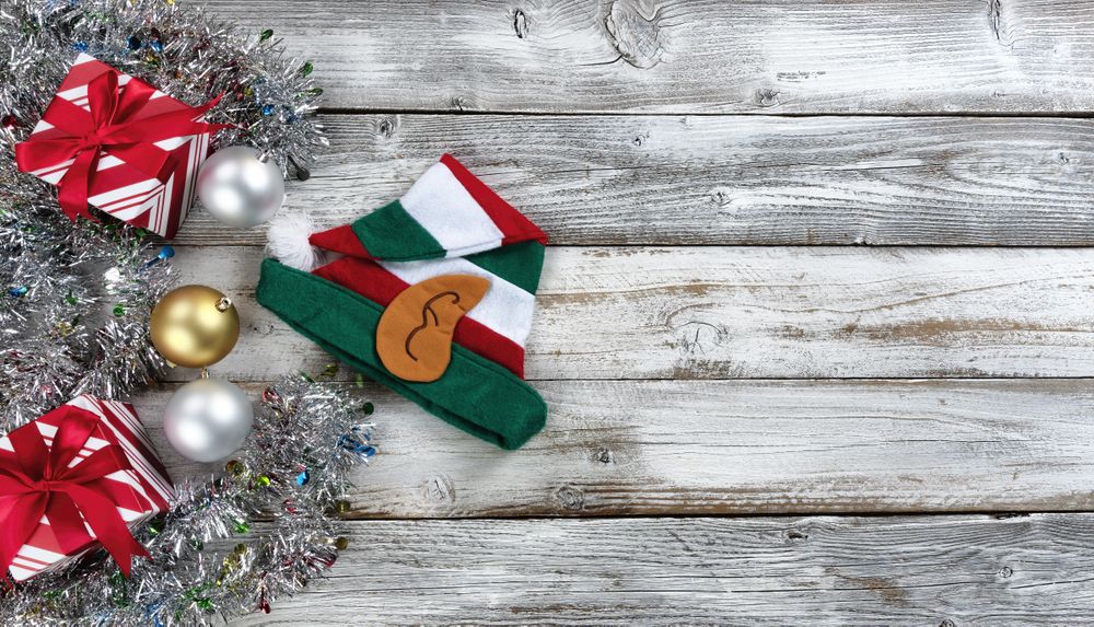 Traditional gold and silver balls, elf cap plus gifts surrounded by tinsel on a wood background for the Christmas or New Year holiday season