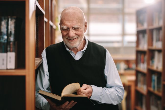 Cheerful older man standing in a library holding a book
