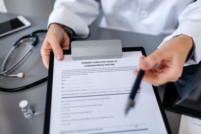 Unrecognizable doctor offering pen to sign coronavirus vaccine consent form
