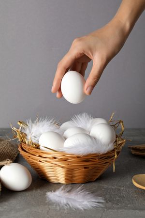 Eggs in a wicker basket, with a hand, on a gray background.