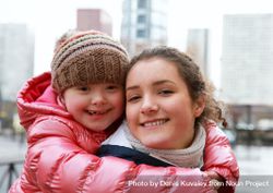 A young girl smiling on her teenager sister’s back on a cold day bYN9N0