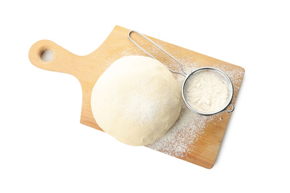Board with dough and flour isolated on blank background