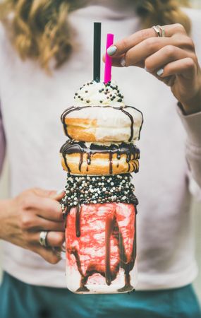 Woman holding stacked donut milkshake with straws, whipped cream, and chocolate sprinkles