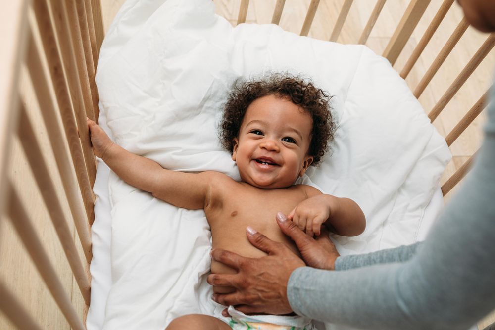 Smiling baby boy lying his crib with his mother holding him