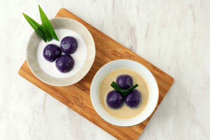 Top view of two bowls of purple sweet potato balls covered in coconut milk sauce