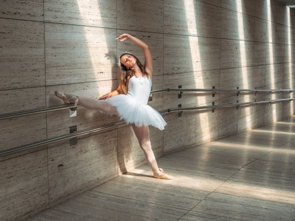 Ballerina doing ballet posing at rail in classroom