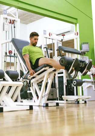 Side view of male in green t-shirt working out quads using gym equipment