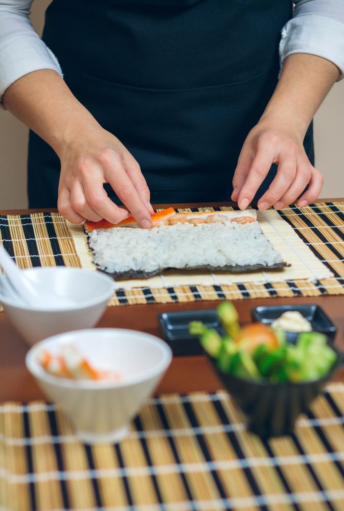 Avocado, cucumber and crab meat bowl in foreground of chef preparing sushi rolls