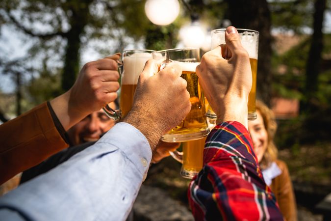 Hands toasting with beer mugs outdoors