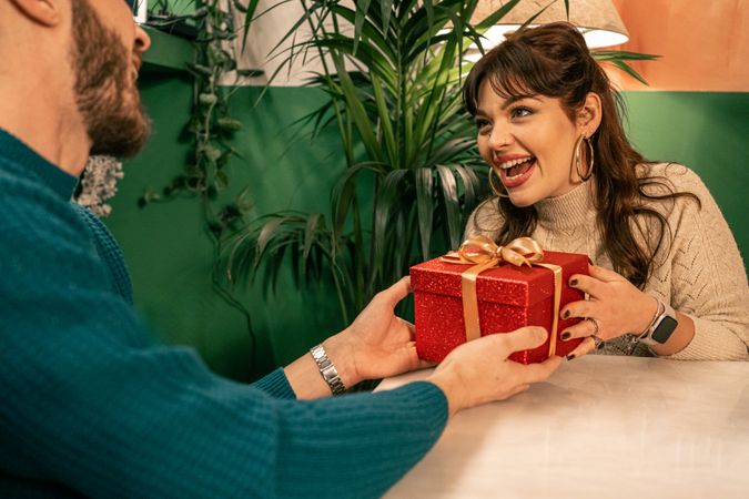 Happy woman with a surprised face receiving a gift from a man during a party