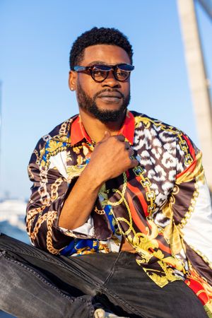 Close up portrait of Black bearded man wearing sunglasses sitting while looking at camera on a sunny day