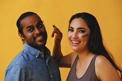 Woman joking while trying to put beauty mask on male friend