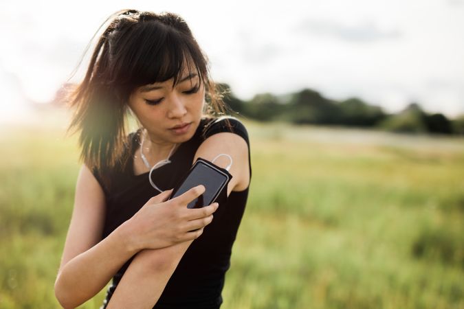 Close up shot of young woman jogger ready to run using smartphone in urban park