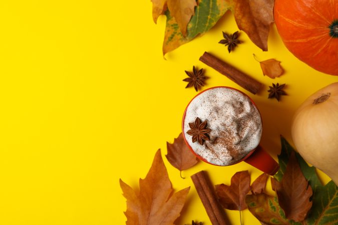 Composition with pumpkin latte, cinnamon, leaves and pumpkin on yellow background