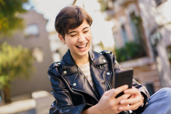 A Cheerful Young Person is Enjoying Their Smartphone While Being Outdoors in Daylight