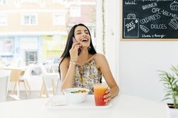 Cheerful woman with healthy food talking on smartphone in cafe