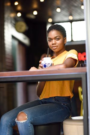 Female sitting with ice tea at counter of modern cafe, copy space