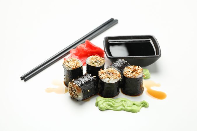Delicious sushi rolls, sauces and chopsticks on plain background, close up