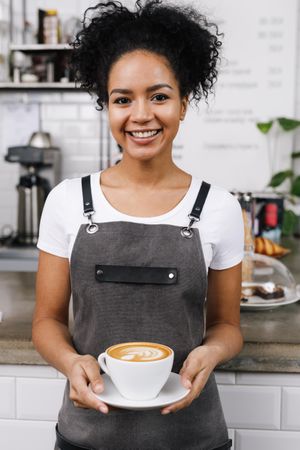 Smiling barista standing and holding cappuccino