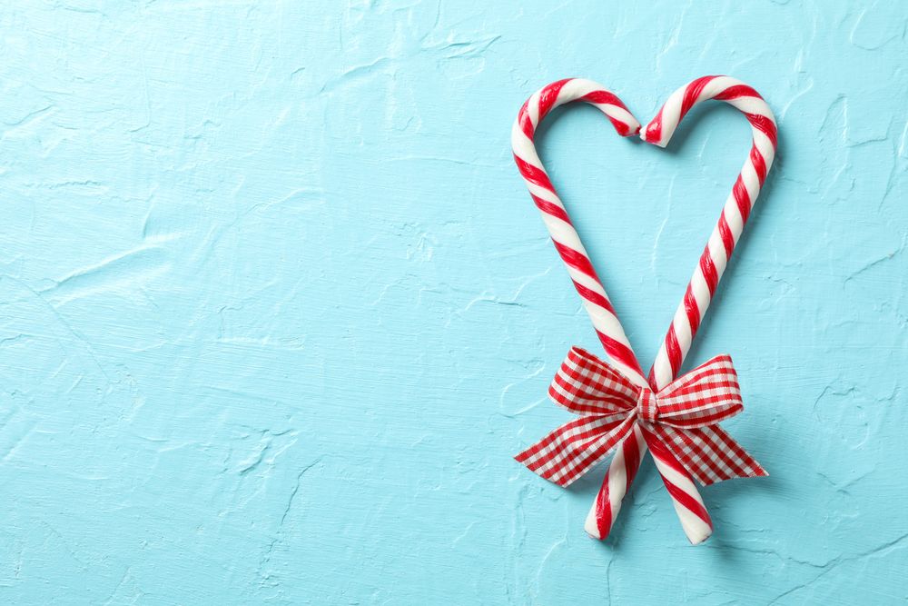 Sweet candy canes with bows on blue background, space for text