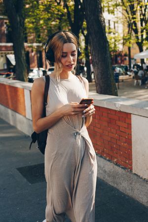 Young woman with headphones and smartphone walking outdoors