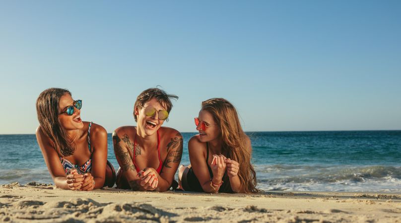 Women on vacation relaxing at the beach wearing sunglasses talking to each other