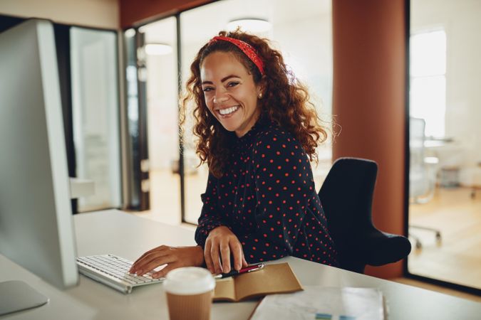 Woman with curly hair smiling at work working at a computer