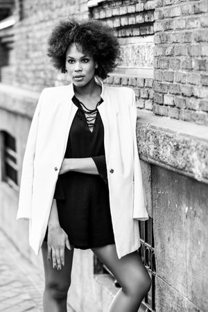 Monochrome shot of female in dress with blazer posing next to outdoor wall