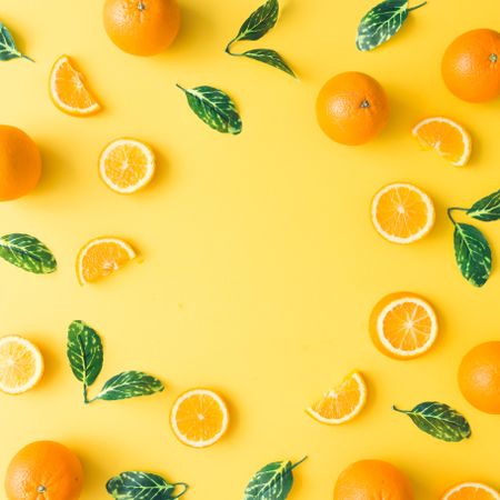 Oranges and green leaves on pastel yellow background