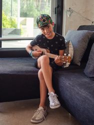 Calm boy playing ukulele sitting on coach