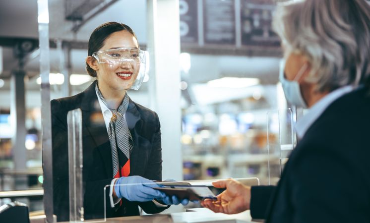 Woman working at check in counter assisting male traveler during pandemic