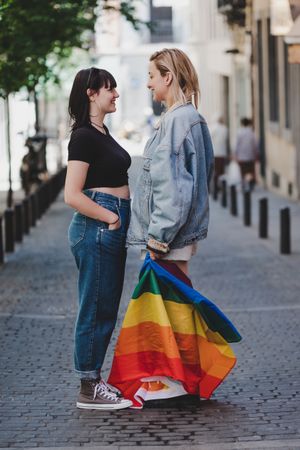 Lesbian couple with LGBT flag standing on street