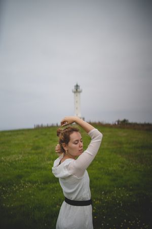Woman walking in green meadow near lighthouse