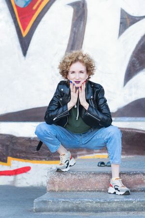 Full length portrait of trendy woman sitting at the graffiti wall background