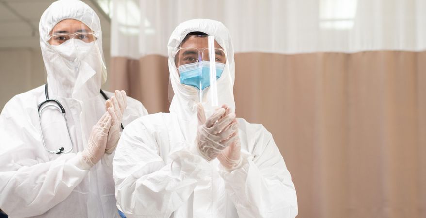 Two male medical professionals in full protective gear clapping hands