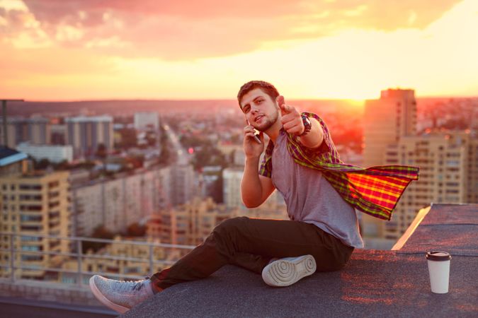 Male taking phone call while looking at camera on roof next to cup of coffee