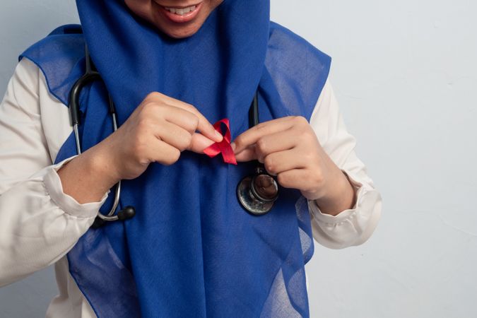 Close up Muslim Female Asian doctor or nurse wearing Red ribbons on cloth, HIV awareness concept, world AIDS day, world cancer day.