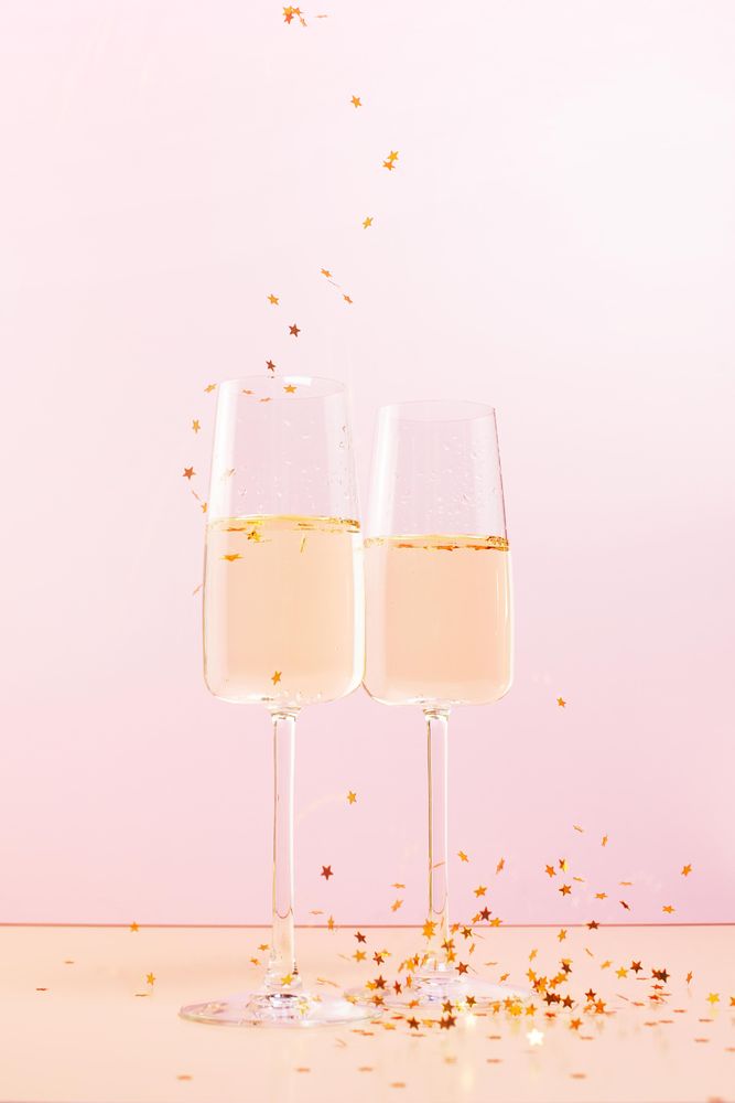 Two glasses of champagne and falling confetti stars on pink background