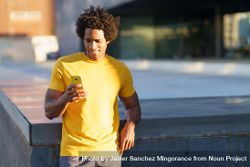 Black man in yellow t-shirt checking his smart phone in the sun 4Be3x5